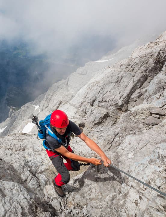 man climbing rock face gripping secure rope
