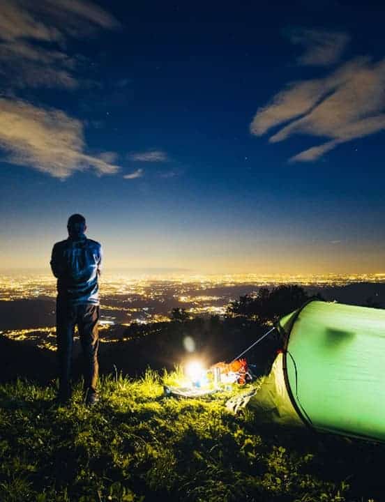 man standing next to tent looking out at illuminated city