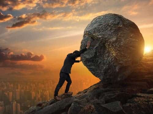 man pushing boulder up hill