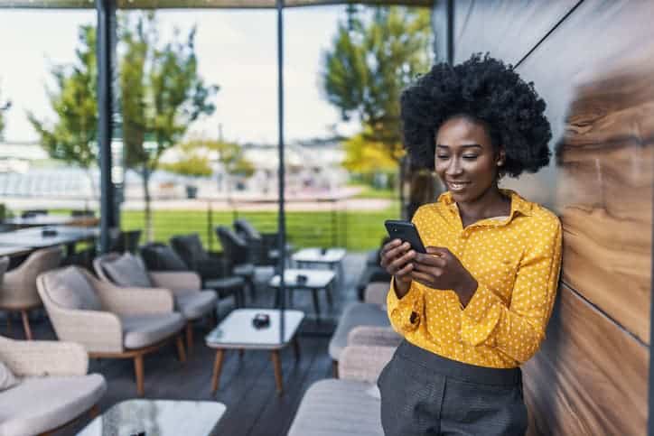 Confident businesswoman texting message outside. Black woman in office suit standing near urban glass wall and using mobile phone. African American business woman concept