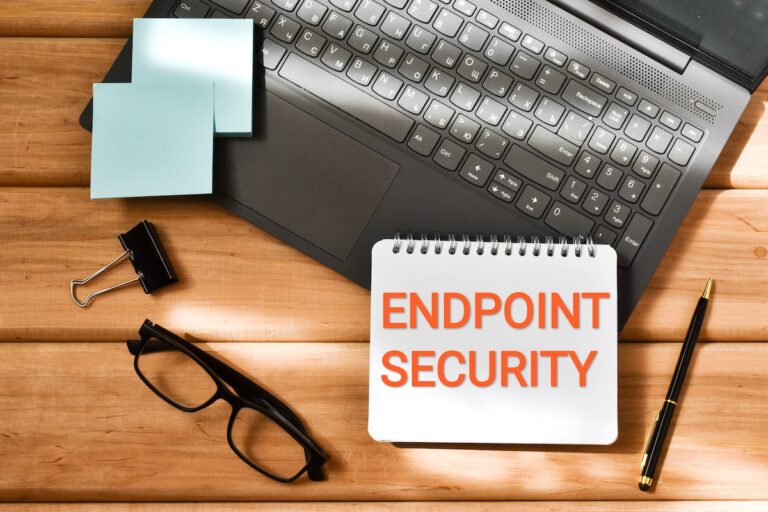 ENDPOINT SECURITY inscription in a notepad near a laptop and eyeglasses on a wooden background.